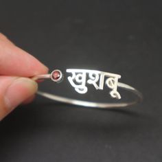 Personalized Hindu Name Bracelet is handmade with its own uniqueness. It can be bought as a gift for any occasion like birthday gift, wedding gift, travel gift, souvenir and etc. If you need rose gold plating or yellow gold plating, please contact us, we will advice you on the additional fees applicable.Base Material: Sterling Silver Size: 11mm (Approximately)Bangle wrist size: 7'' - 8'' Inches. Adjustable / Please give us your wrist circumference.Stone: Red CZ setting (Default) Or check with us Name Bangle Bracelet For Valentine's Day Gift, Valentine's Day Gift Name Bangle Bracelet, Unique Red Bracelet As Gift, Unique Red Bracelet For Gift, Sterling Silver Name Bracelets For Wedding, Custom Name Sterling Silver Bracelets For Wedding, Personalized Red Jewelry For Birthday Gift, Adjustable Birthstone Name Bracelet As A Gift, Customized Bangle Name Bracelet As Gift