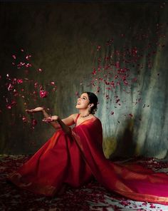 a woman in a red dress sitting on the ground with petals falling from her hands