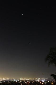 the night sky is lit up with bright lights and some trees in front of it