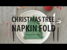 a white plate topped with a christmas tree napkin fold on top of a wooden table