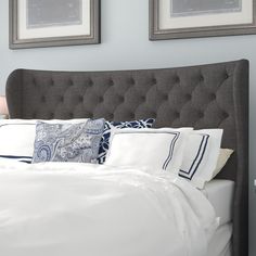 a bed with white sheets and pillows in a bedroom next to two framed pictures on the wall