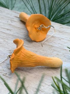 two yellow earrings are sitting on a wooden table next to some green plants and pine needles