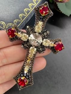 a person holding a cross shaped brooch with red and yellow stones on it's side