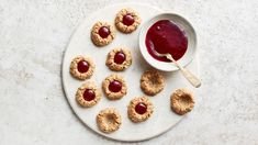 peanut butter and jelly cookies on a white plate with a bowl of jam in the middle