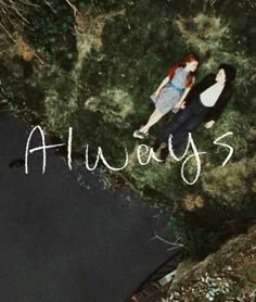 an aerial view of two people laying on the ground next to some water and grass