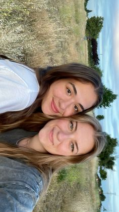 two women are standing next to each other in front of the water and grass area