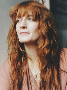 a woman with long red hair and blue eyes looks up at the camera while wearing a pink shirt