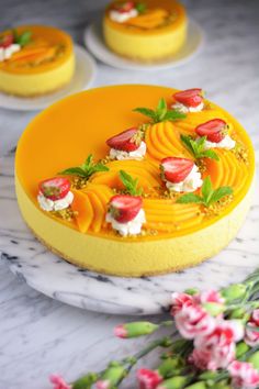 there is a yellow cake with strawberries on the top and flowers in the background