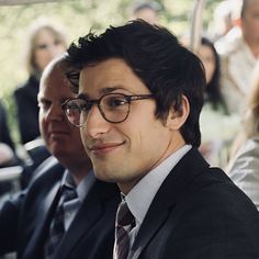 a man wearing glasses sitting next to other people