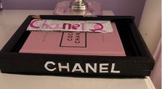 a chanel perfume bottle sitting on top of a black and pink box next to a silver faucet