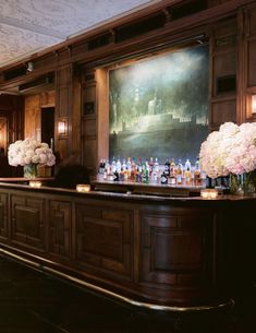 a bar with flowers and bottles on it in front of a large painting hanging above the bar