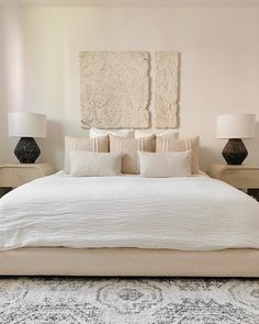 a white bed sitting in a bedroom next to two black and white lamps on either side of the bed