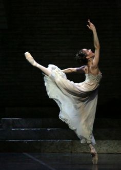 a ballerina is performing on stage with her arms in the air while wearing a flowing white dress