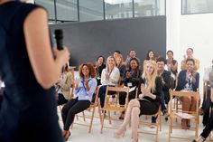 a group of people sitting in chairs with one woman holding a microphone and the other standing up