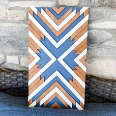 a blue and white geometric design on wood sitting next to a brick wall in front of a stone wall