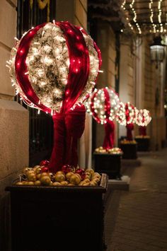 christmas lights are on display in front of a building with red and white balls hanging from it's sides