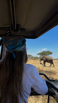 a woman is looking at an elephant in the distance while riding on a safari bus