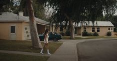 a woman walking down the sidewalk in front of a house