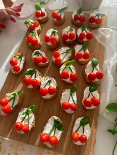 small appetizers with cherry tomatoes and cream cheese are arranged on a cutting board