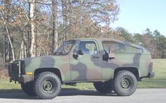 a camo truck parked on the side of the road in front of some trees