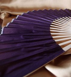 a purple fan sitting on top of a bed next to a satin material pillow cover