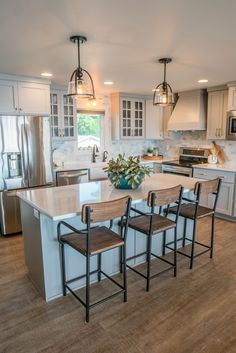 a kitchen with white cabinets and wooden flooring, an island in the middle is surrounded by four stools