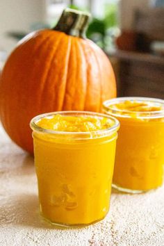 two jars filled with orange colored liquid next to a pumpkin