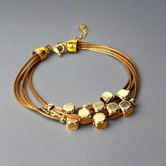 Get ready to elevate your wrist game with this multi-strand leather bracelet. Featuring gold-plated floating beads and a lobster clasp closure, this timeless piece is the perfect way to add a touch of sophistication to any outfit. Length: 6.5" + 1.5" extender chain Lobster clasp closure - for a secure fit 6 strands of brown leather - for the perfect boho vibe 18K PVD Gold plated stainless steel - long lasting plating and hypoallergenic Handmade in China - to bring you the best possible price Thi Adjustable Gold Leather Bracelet Chic Style, Adjustable Gold Leather Chic Bracelet, Adjustable Gold-tone Metal Beaded Bracelet, Modern Multi-strand Gold Jewelry, Modern Gold Multi-strand Jewelry, Adjustable Gold Bracelets For Accessorizing, Adjustable Multi-strand Metal Bracelets, Gold Adjustable Double Strand Beaded Bracelets, Modern Gold Beaded Metal Bracelets