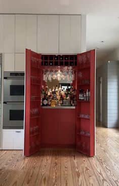 an open red cabinet in a kitchen filled with bottles and glasses