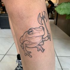 a frog tattoo on the leg with a spear in it's mouth and eyes