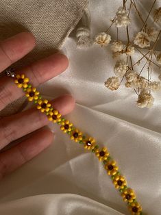 a hand holding a beaded yellow and green bracelet next to flowers on a white cloth