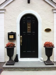 two large black pots with flowers on the front step of a house that is painted white