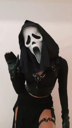 a woman in a black outfit with a white mask on her face and hands behind her head