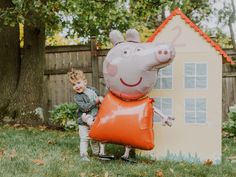 a little boy standing next to an inflatable peppo pig house and balloon