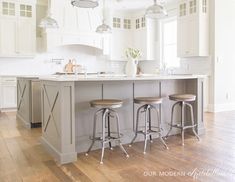 three stools sit at the center of a large kitchen island with white cabinetry