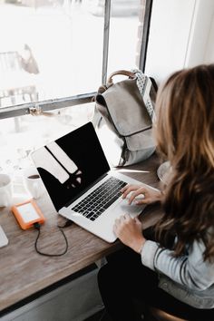 a woman sitting at a table with a laptop computer in front of her, looking out the window