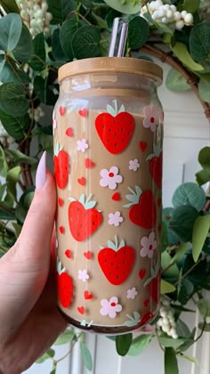 a hand holding a mason jar with strawberries on it and flowers around the lid