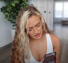 a woman is looking at her cell phone in the living room while wearing a white tank top