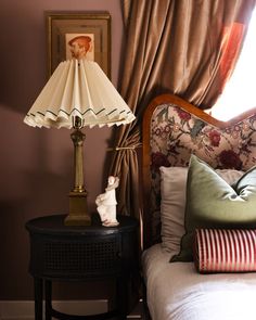 a lamp on a nightstand next to a bed in a room with pink walls and curtains