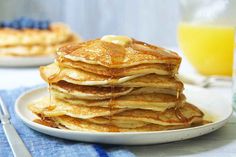 a stack of pancakes sitting on top of a white plate next to a glass of orange juice