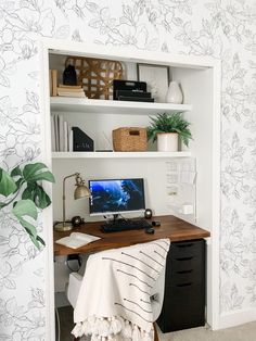 a desk with a computer on top of it next to a potted plant and bookshelf