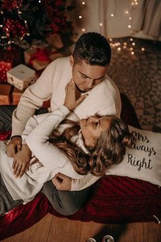 a man and woman sitting on the floor in front of a christmas tree with presents