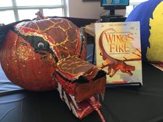 there is a book about wings in the fire next to a pumpkin and an animal head