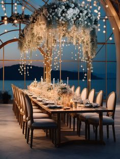 a dining table with white flowers and candles on it in front of a large window