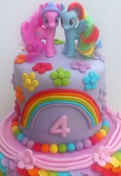 a birthday cake with two little ponys on top and flowers around the edges, all decorated in rainbow colors