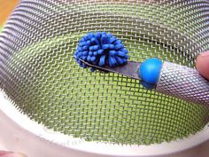 a person is holding a blue and white brush in a strainer net bowl with a green background