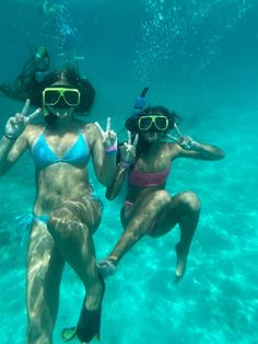 two women in bikinis and snorkels pose for the camera under water