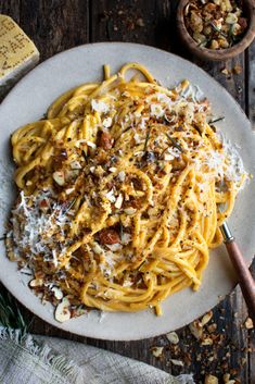 a white plate topped with pasta covered in parmesan cheese and nuts next to a wooden spoon