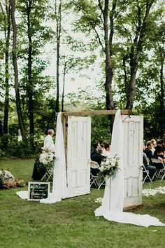 an outdoor wedding ceremony with white drapes and greenery on the grass, surrounded by trees