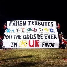 a group of people holding up a sign in front of a field at night time